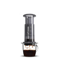 Aeropress coffee maker dispensing coffee into a glass mug on a white background