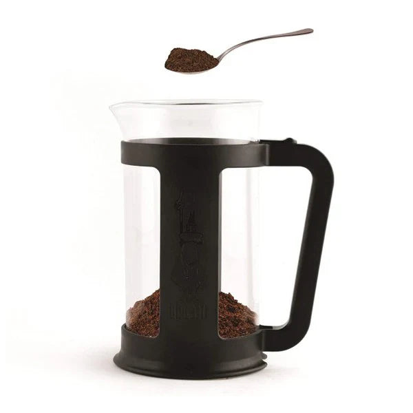 Black French press with coffee grounds and a spoonful of coffee on a white background