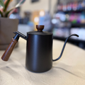 Black teapot with wooden handle and lid on a light surface