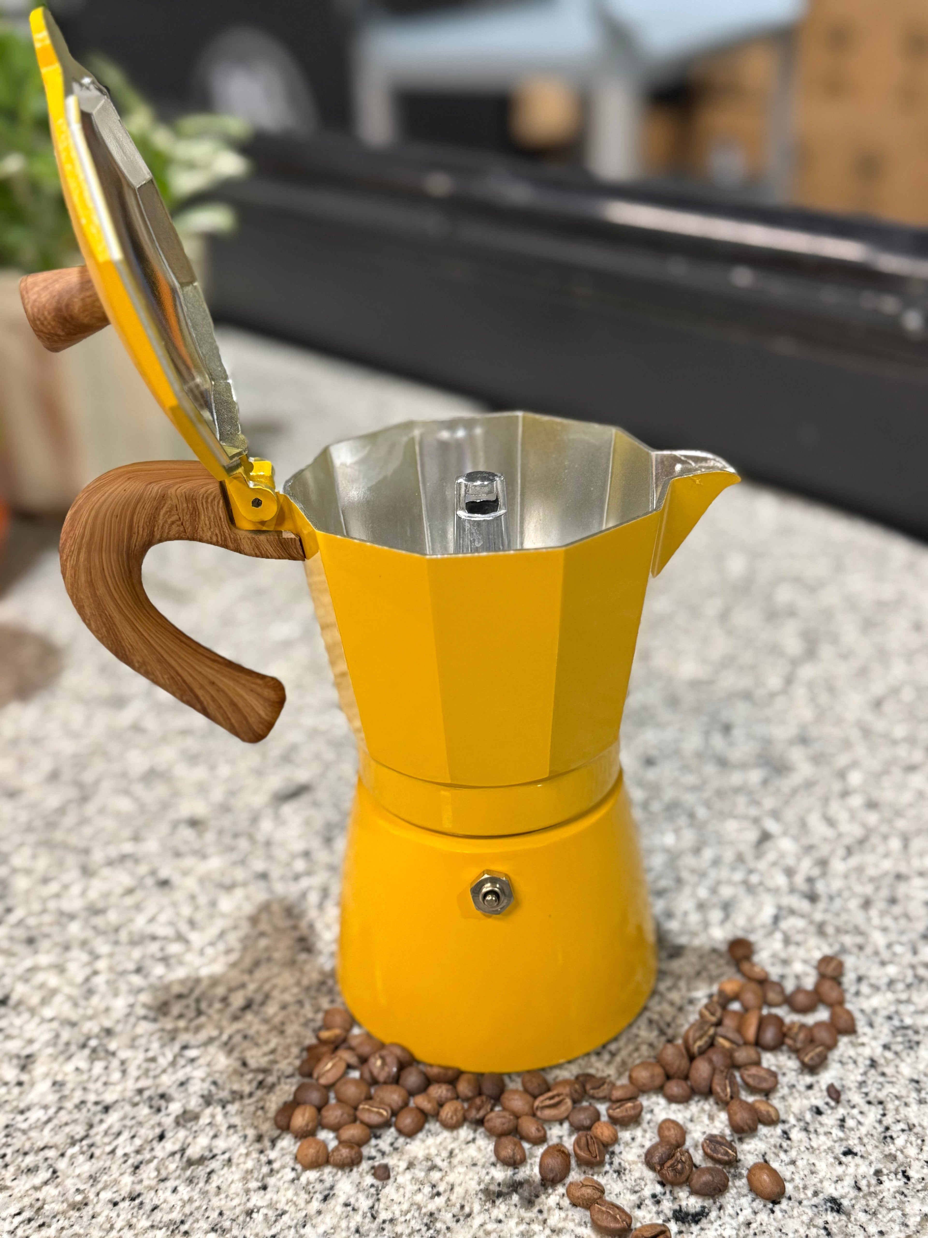 Yellow espresso maker with wooden handle on a surface with coffee beans around