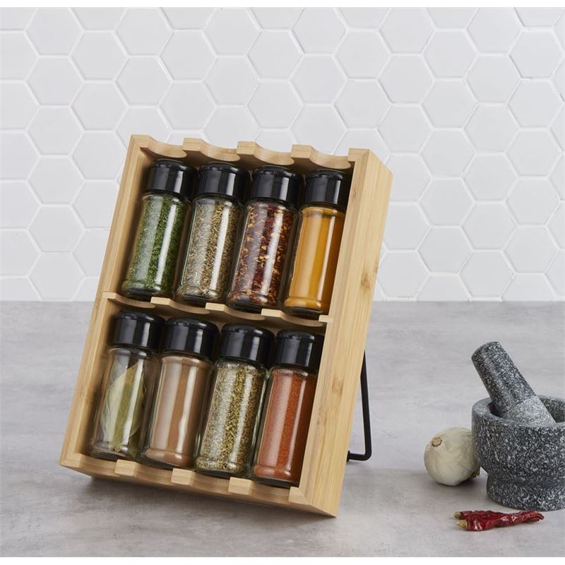 Wooden spice rack with black lids containing various spices on a kitchen counter.